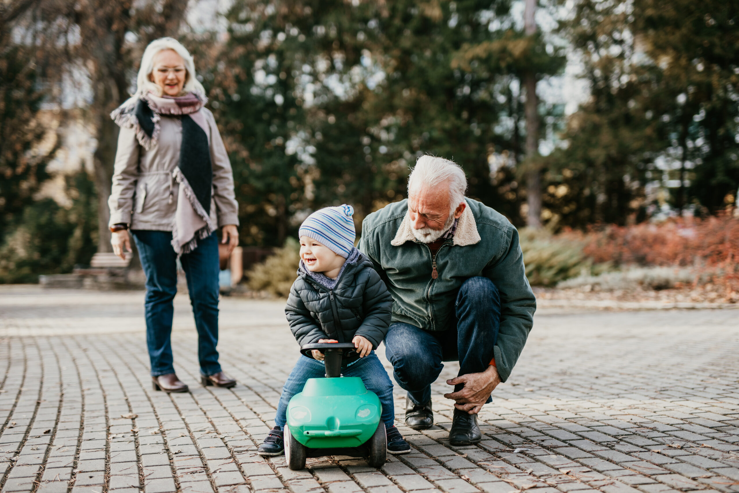 Happy good looking senior couple husband and wife walking and playing with their adorable grandson in public city park