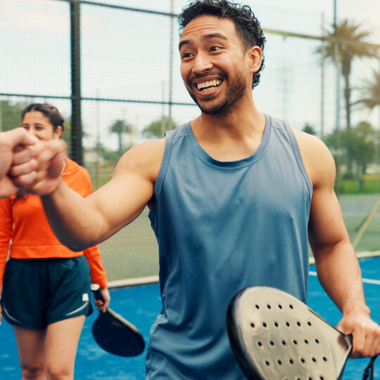 Men, fist bump and padel with smile, sports and respect with support, challenge and excited for game. People, athlete and happy with greeting at tennis court, exercise or contest at fitness club We can help get you back to doing what you love.